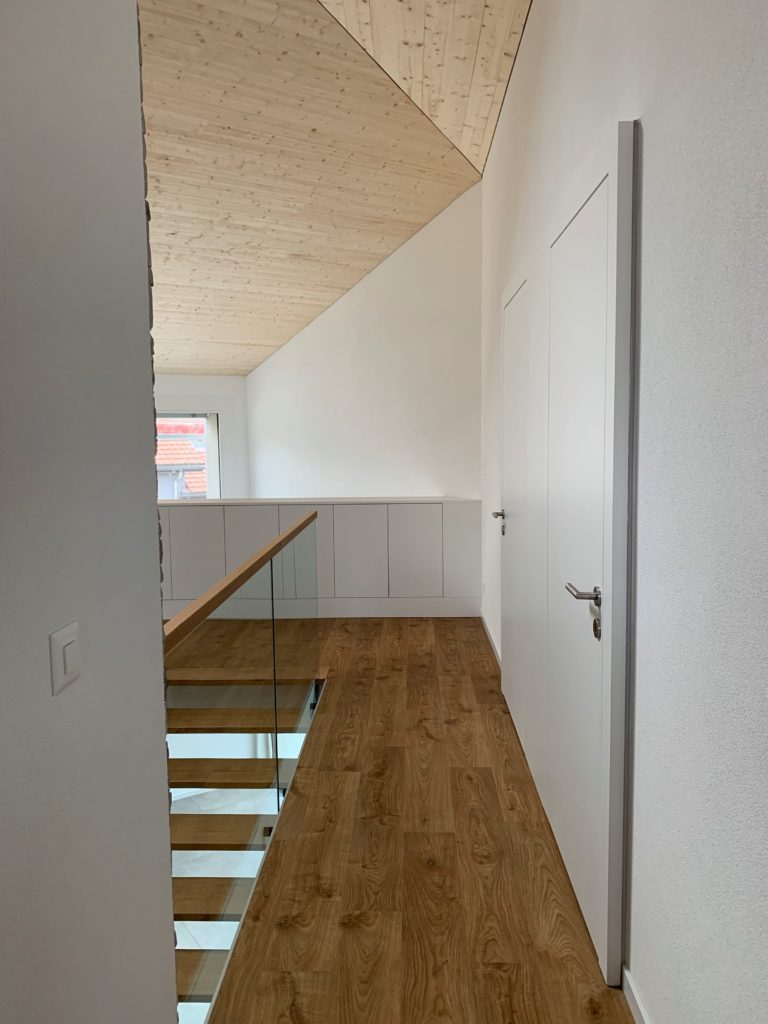 Couloir intérieur rénové avec escalier, garde-corps vitré et parquet